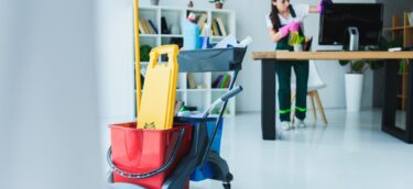 young female janitor cleaning office with various cleaning equipment