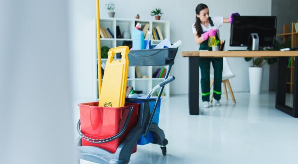 young female janitor cleaning office with various cleaning equipment