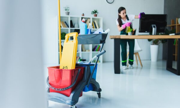 young female janitor cleaning office with various cleaning equipment